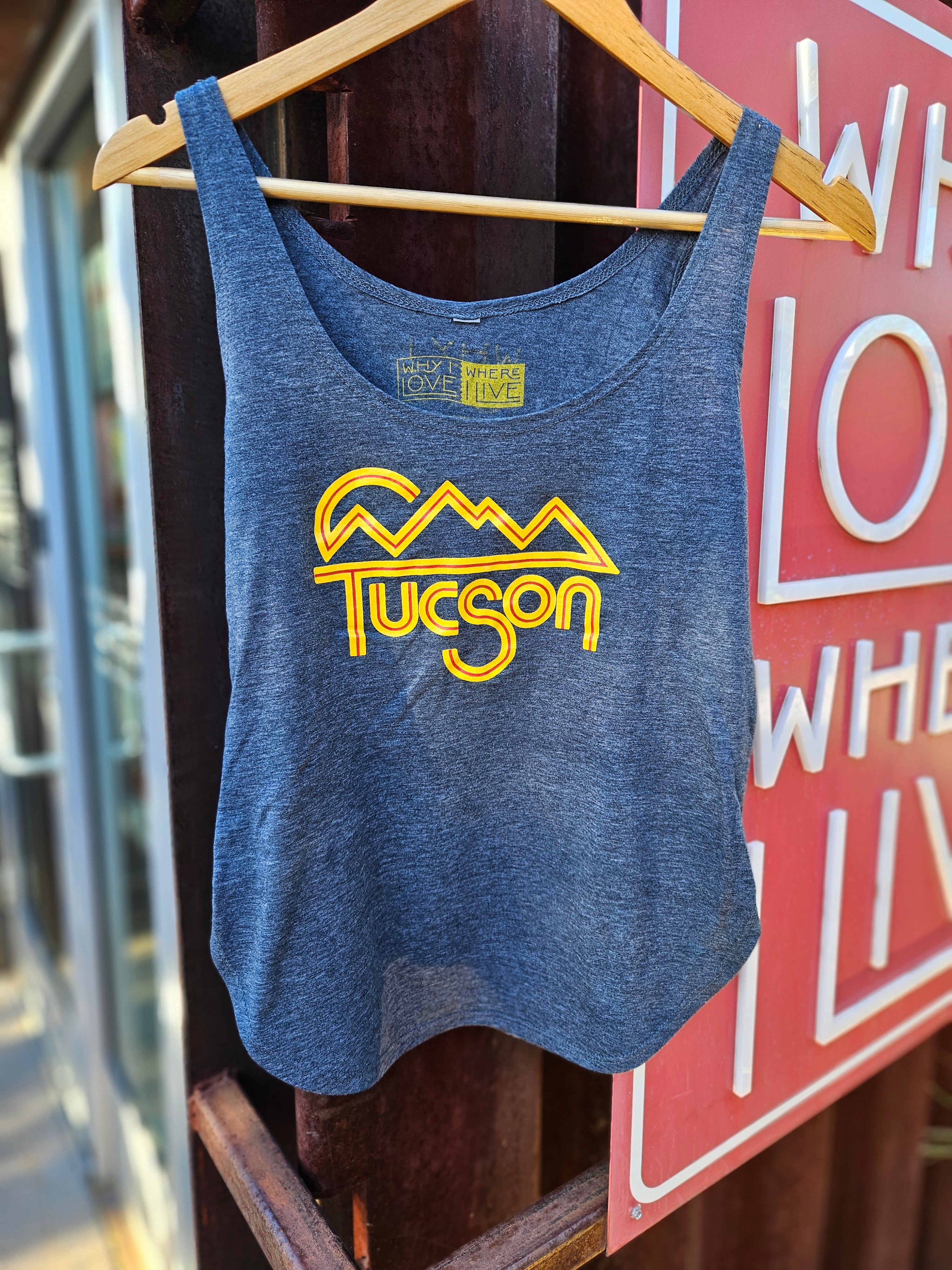 Blue tank top with yellow 'Tucson' design hanging on the surface of a shipping container